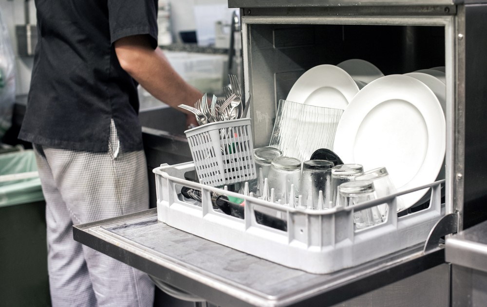 a man working in a commercial kitchen prepares to unload and then clean a commercial dishwasher