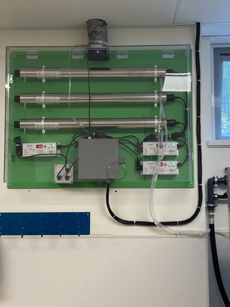 a lux laundry system mounted to a wall in bc business laundry facility with uv tubes and power boxes mounted on a green backboard